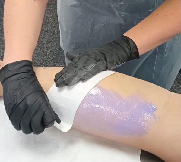 Therapist in gloves applying wax strip to a leg